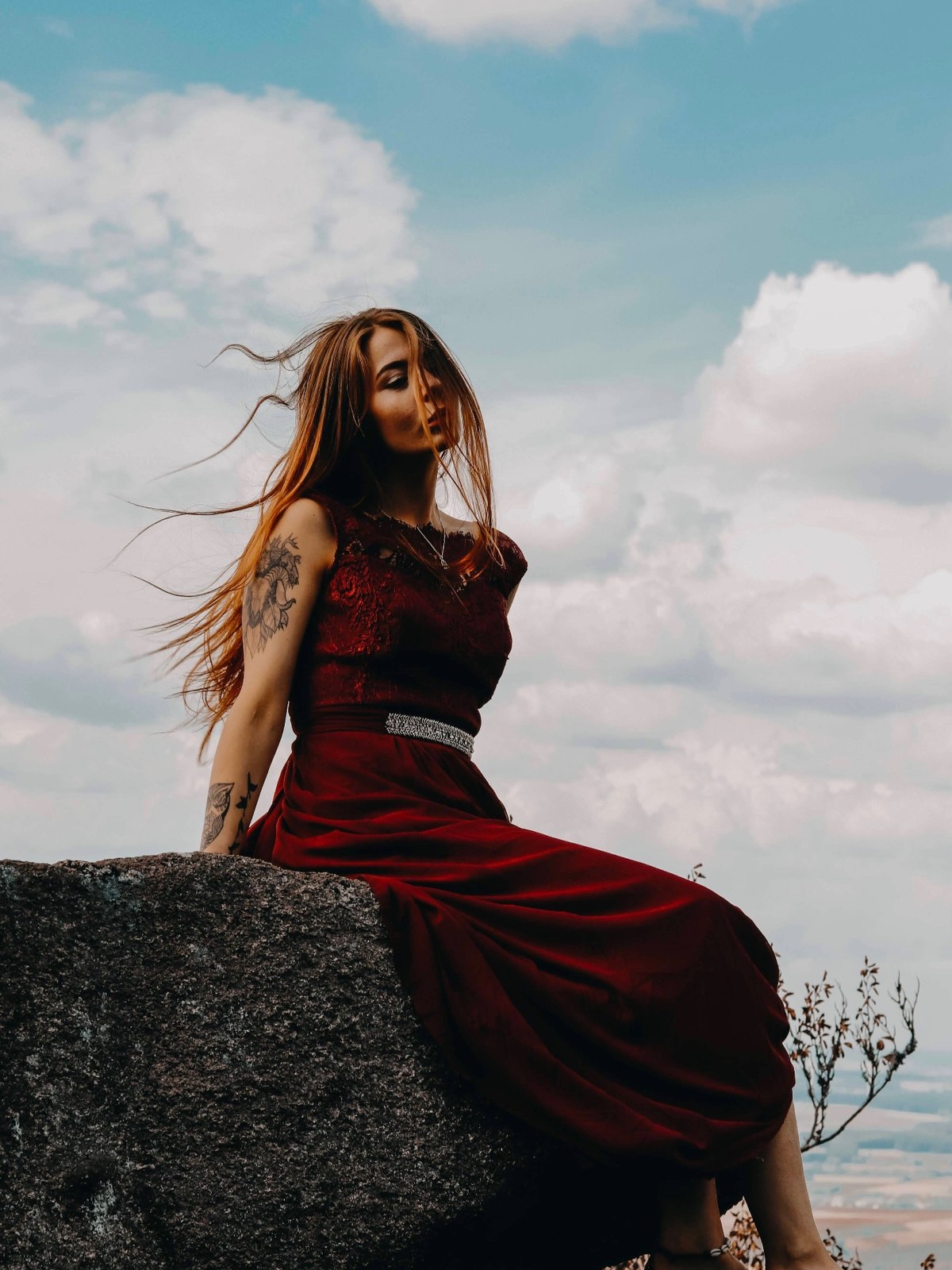 byliv in a red gown seated on a rock against the sky